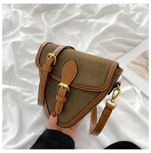 Detalle de bolso bandolera triangular de ante marrón con hebillas doradas y acabados en piel