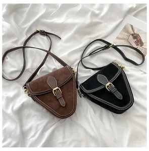 Detalle de bolsos bandolera triangulares de ante con costuras en contraste y hebilla