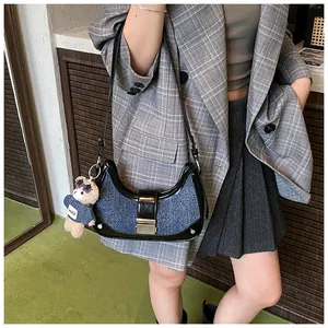 Detail of denim and leather crescent bag featuring a stylish brown bear charm