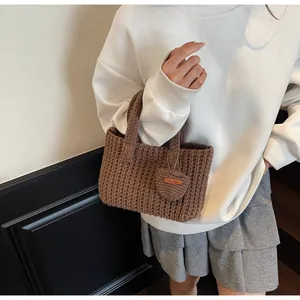 Détail du sac à main crocheté marron foncé avec breloque cœur sur une jupe plissée grise
