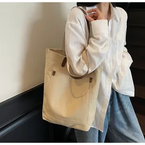 Spacious off-white canvas tote bag with brown leather straps worn by a model