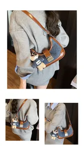 Detail of blue denim crescent bag with brown leather trim and a cute bear keychain charm