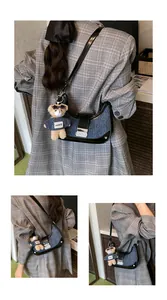 Detail view of denim crescent shoulder bag with leather trim and bear pendant decoration