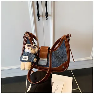 Detail of denim and brown leather patchwork crescent bag with a cute teddy bear charm