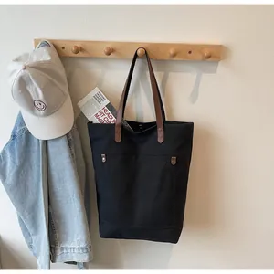 Detail of black canvas tote bag with brown leather strap and vintage metal rivets