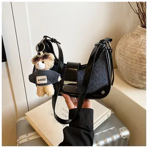 Detail of denim crescent hobo bag with silver buckle and bear charm in urban setting