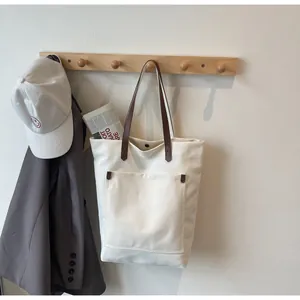 Detail of canvas tote bag with brown leather straps and metal rivets on a wooden hanger