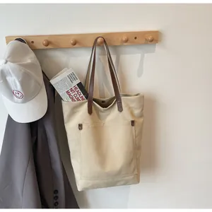 Close-up of beige canvas tote bag with brown straps and metal rivet pocket detail