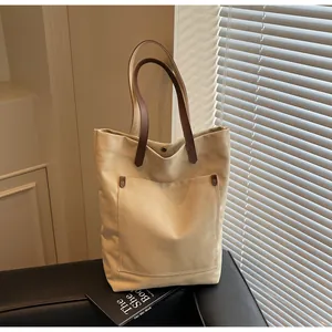 Detail of canvas tote bag featuring premium brown leather handles and metal rivet fasteners