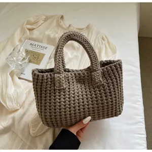 Vue macro montrant la texture gaufrée marron foncé et la poignée artisanale du sac en tricot