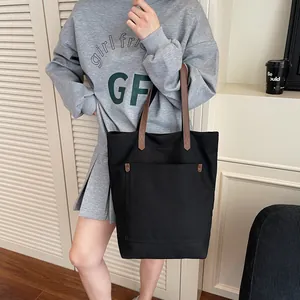 Large black canvas tote bag with brown handles and front pocket for casual commute