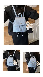 Detail eines hellblauen Denim-Minirucksacks mit Drehverschluss und Plüschbär-Anhänger
