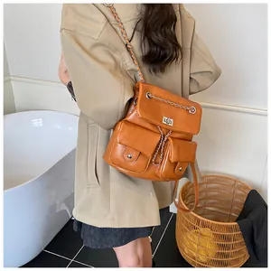 Detail of tan leather backpack with metal chain straps and front pockets in a lifestyle setting