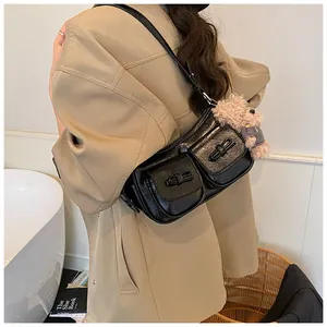 Detail of black glossy shoulder bag with bow accents and a plush bear pendant charm