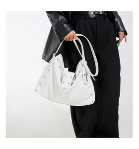 Detail van witte hobo-tas met zilveren studs en een metalen kruisvormige hanger