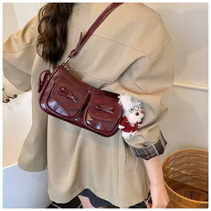 Detail of burgundy shoulder bag with dual front pockets and plush teddy bear charm