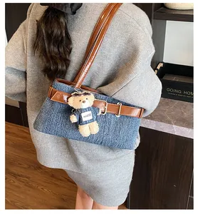 Detail der blauen Denim-Umhängetasche mit braunem Lederriemen und Teddybär-Anhänger