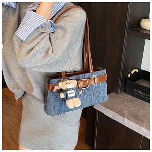 Detail der Schultertasche aus Denim mit Lederriemen und süßem Teddybär-Anhänger
