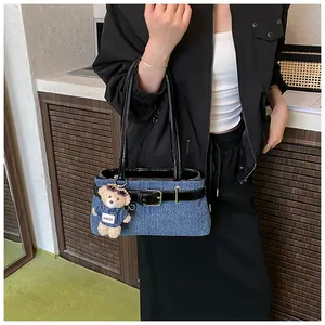 Detail der blauen Denim-Tasche mit glänzendem Lederriemen und Teddybär-Anhänger