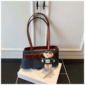 Detail der blauen Denim-Tasche mit braunen Lederriemen und süßem Plüschbären-Anhänger