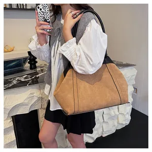 Detalle de un bolso tote grande de ante marrón con adornos de cuero negro y base reforzada