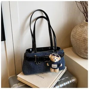 Detail der blauen Denim-Schultertasche mit Lederriemen und süßem Bärenanhänger