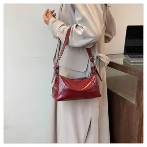 Detailed side view of deep red shoulder bag with functional zipper pocket on beige trench coat