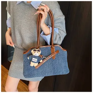 Detailansicht der Denim-Tasche mit braunen Lederriemen und Plüschbär-Anhänger am Griff