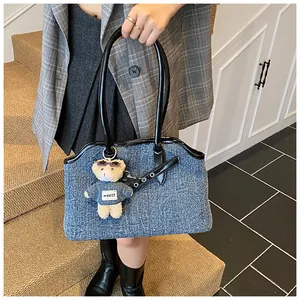 Detail der Denim-Einkaufstasche mit schwarzen Ledergriffen und süßem Teddybär-Anhänger