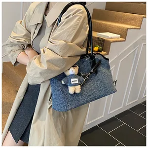 Detail der blauen Denim-Tragetasche mit schwarzen Lederriemen und einem Teddybär-Anhänger