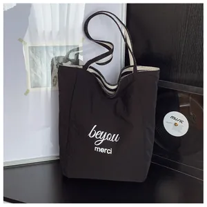 Dettaglio della borsa tote in tela nera con testo merci bianco e tracolla a righe