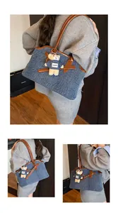 Detail der blauen Denim-Tragetasche mit braunen Ledergriffen und einem Teddybär-Anhänger