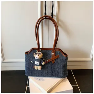 Detail der blauen Denim-Tasche mit braunen Ledergriffen und einem Bären-Anhänger