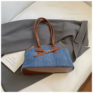 Detail der Denim-Handtasche mit braunem Leder auf grauem Blazer und einem Buch
