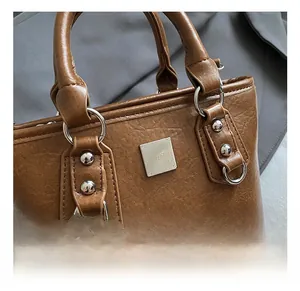 Detailed close-up of brown bucket bag showing silver rivets and metal logo plate