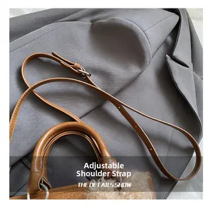 Detail of adjustable brown faux leather shoulder strap with metallic buckle on bucket bag