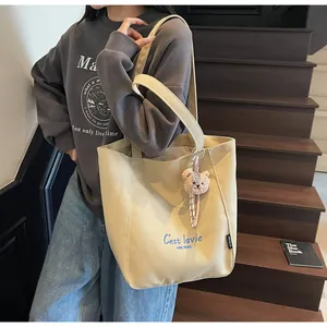 Detail of beige canvas tote bag with blue C'est la vie lettering and teddy bear charm