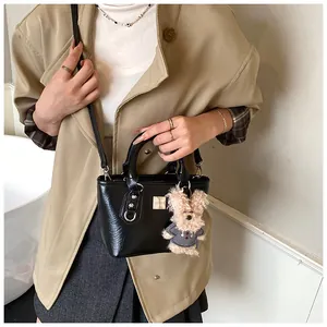 Close-up of black leather bucket bag with cute plush bear charm and metallic logo