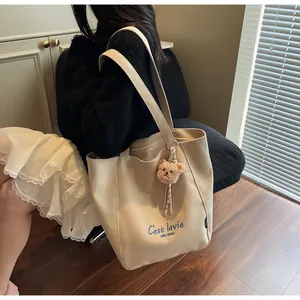 Close-up of cream canvas tote bag with navy blue embroidery and plush bear charm decoration