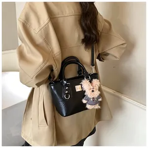 Detail of black textured leather bucket bag with plush bear charm and chain strap