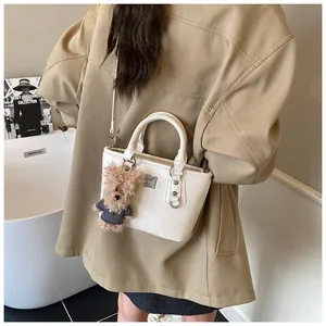White textured leather bucket bag featuring a cute brown bear charm and metal logo detail