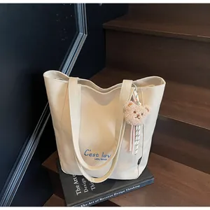 Detail of off-white canvas tote bag with blue embroidery and cute brown plush bear charm