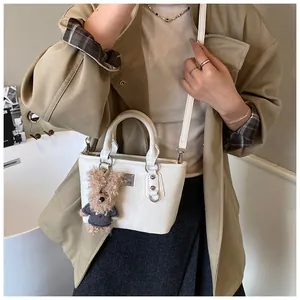 Close-up of a white bucket bag with textured leather and a cute plush bear pendant