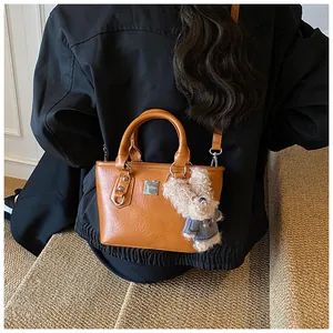 Detail of a brown bucket bag featuring a plush doll charm and a silver brand plate