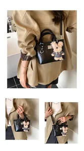 Detail view of black lychee texture leather bucket bag with a cute brown teddy bear charm
