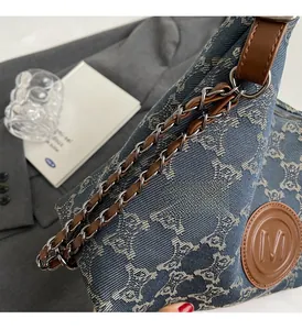 Close-up of denim tote bag featuring monogram pattern and silver metal chain strap