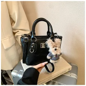 Black leather bucket bag with a cute teddy bear charm on a minimalist suitcase background