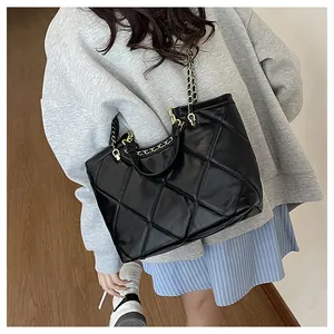Detail of black quilted tote bag with chain strap shown on a person for size