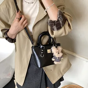 Minimalist black leather bucket bag with gold bear charm and adjustable shoulder strap