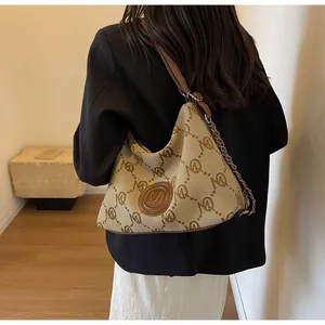 Detail of canvas hobo bag with monogram pattern and leather chain strap on model